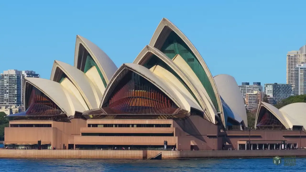 The Sydney Opera House shells seen from the water on a clear day, with harbourside apartment towers behind.